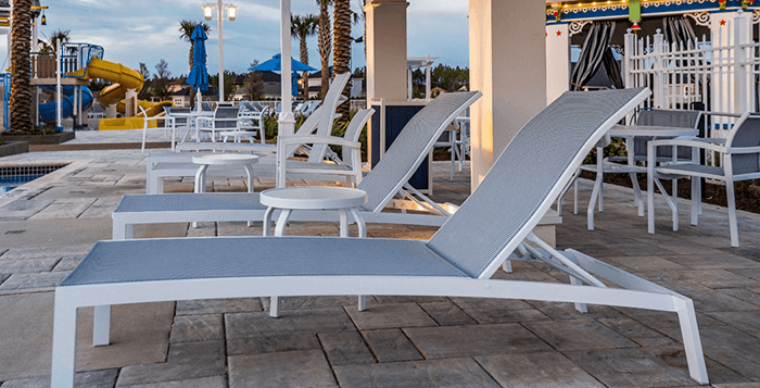 Commercial sling chaise lounges on a resort-style pool deck with modern outdoor seating and waterpark amenities in the background.